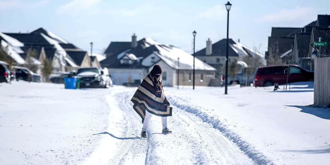 A man walks to his friend's home in a neighborhood without electricity as snow covers the BlackHawk neighborhood in Pflugerville