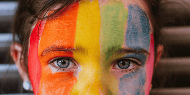 Close up on a young girls face that is painted rainbow