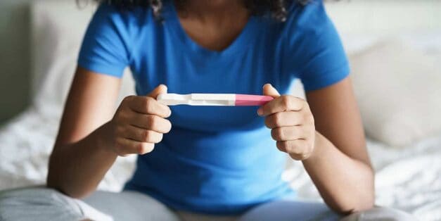 Women holding a Pregnancy Test sitting on the bed