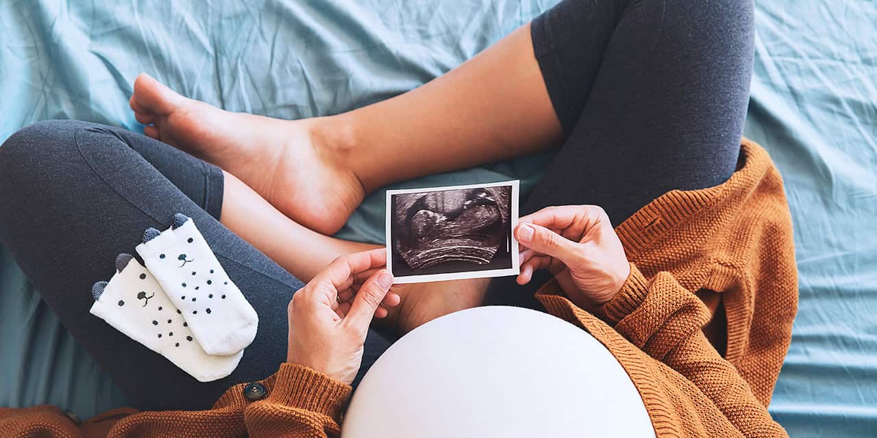 Pregnant woman sitting and holding a photo of her ultrasound next to her growing belly