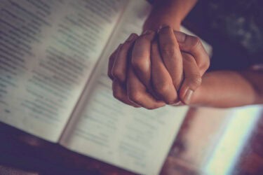 Folded Prayer Hands Over Bible